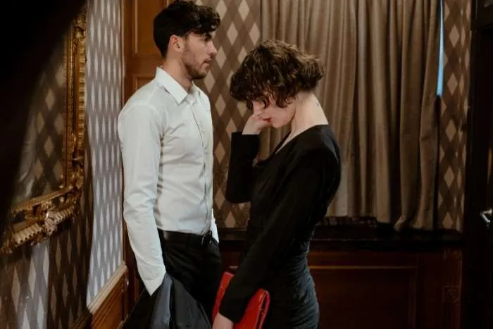 Man standing beside woman, woman looking down with hand on face.