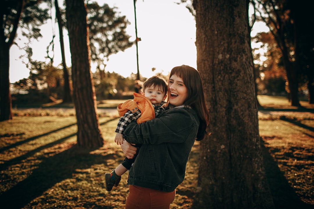 woman in black jacket and blue denim shorts standing beside brown tree during daytime