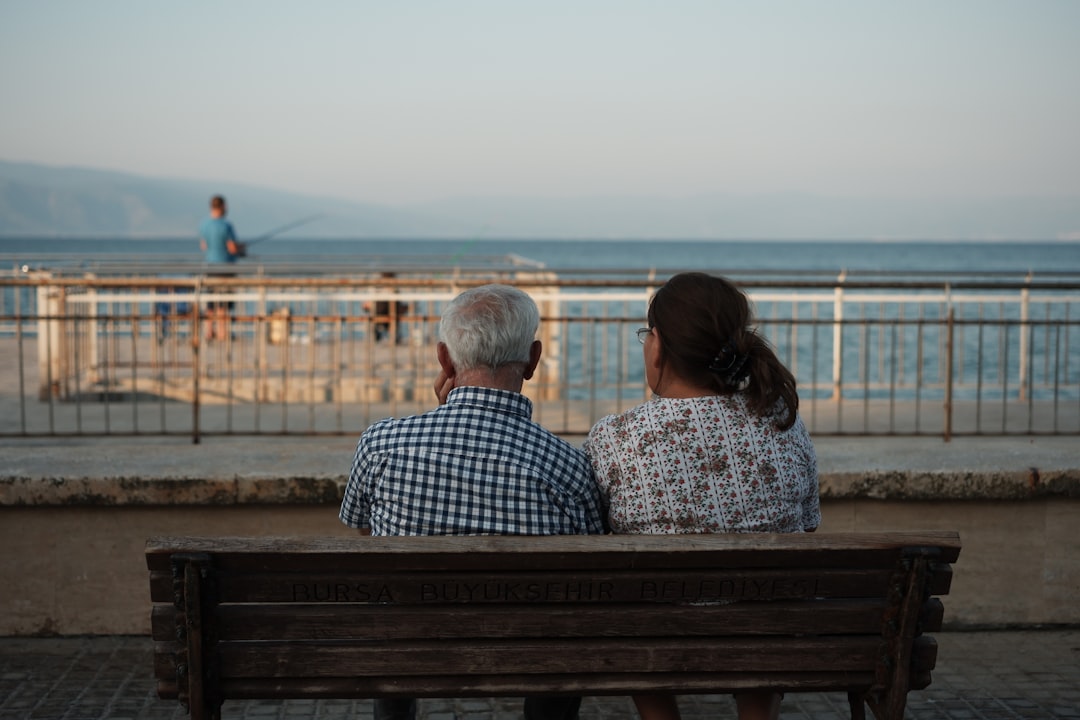 a man and a woman sitting on a bench looking at the ocean